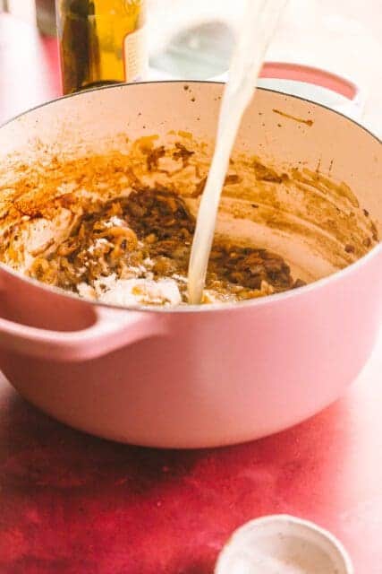 pouring broth into a pot for French onion chicken