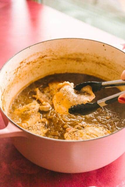 Tongs lifting French onion chicken out of the pot