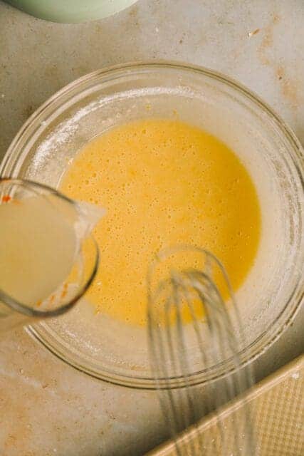 pouring lemon juice into ingredients to mix together for lemon bar recipe