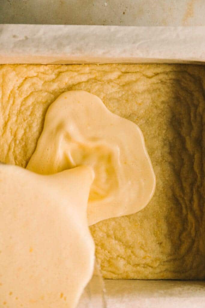 pouring lemon filling on top of baked crust for lemon bars