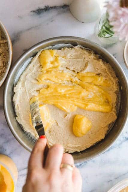 spreading lemon curd on top of lemon cake batter in a cake pan
