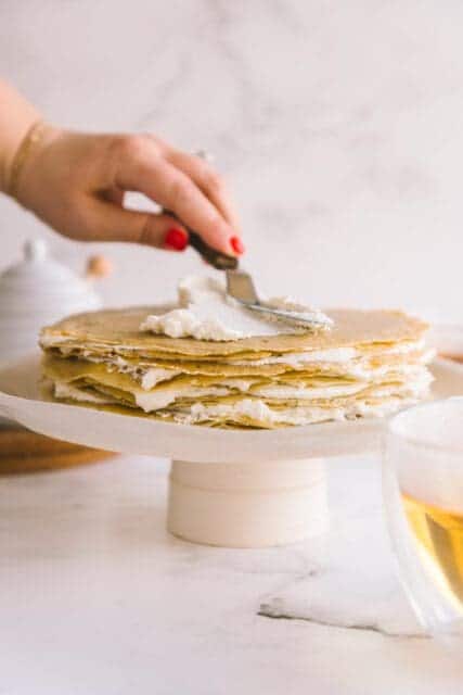 spreading soft whipped cream on layers of crêpes