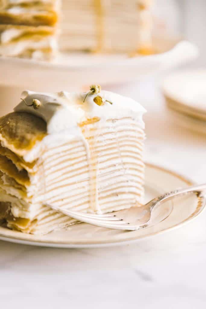a slice of crêpe cake on a white plate with gold markings and a silver fork