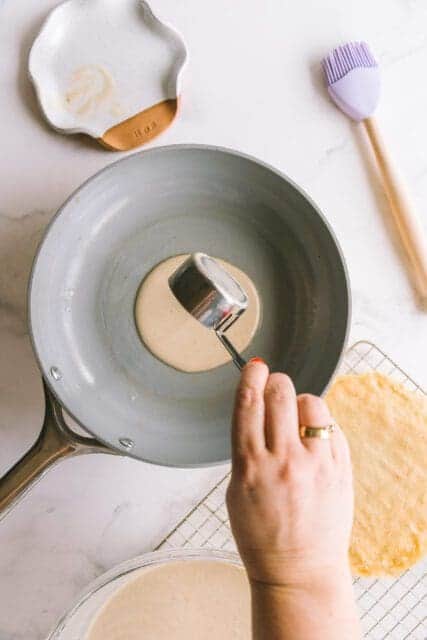 pouring crêpe batter into a hot frying pan
