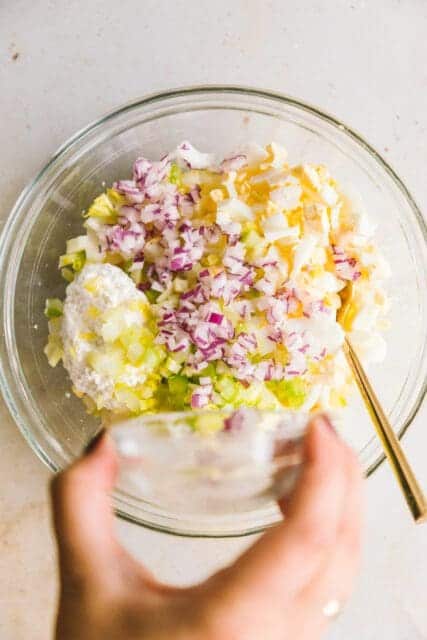 adding duke's mayonnaise, salt and red onions to the hard boiled eggs