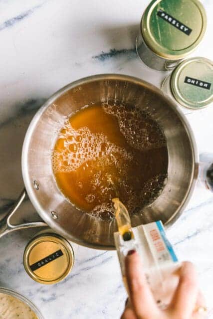 pouring stock into a bowl to make au jus for the french dip sandwich