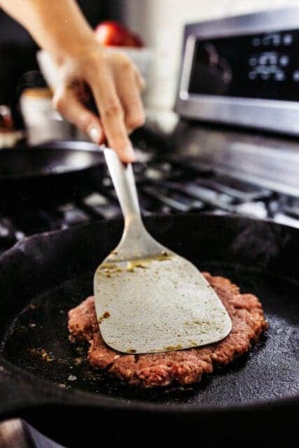 smashing ground beef in a cast iron pan for smash burger recipe
