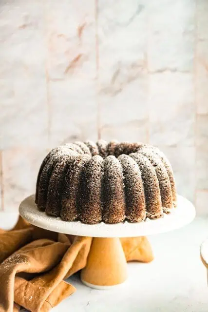 The Perfect Chocolate Bundt Cake, dusted with powder sugar displayed on a white cake plate.