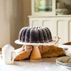 A Chocolate Bundt Cake on a Ceramic cake plate on top of a Marble countertop