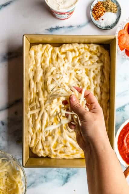 sprinkling cheese on top of the focaccia pizza