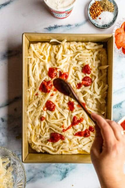 dolloping marinara sauce on top of cheesy focaccia