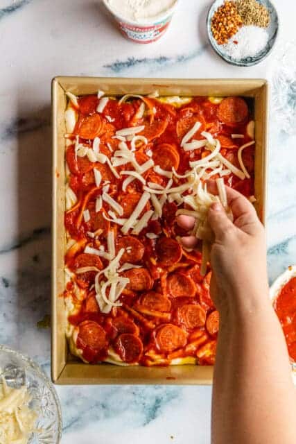 topping the focaccia pizza with more cheese before it bakes in the oven