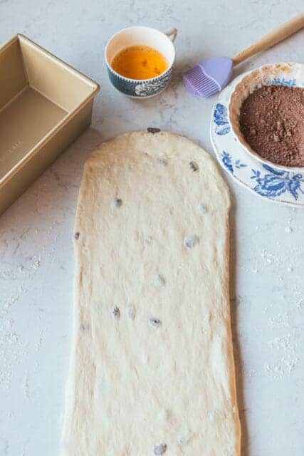 rolled out raisin bread dough with cinnamon swirl ingredients ready to be added