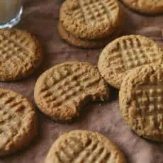 a dozen peanut butter cookies laid out on a mauve linen with a glass of milk