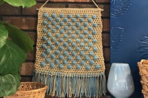 Handmade macrame wall art with blue and beige yarns.