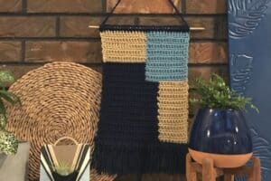 Handwoven wall hanging with geometric patterns in beige, blue, and black.