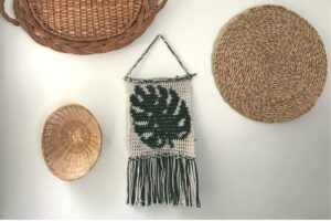 Handwoven wall hanging with green leaf design and fringe detail.