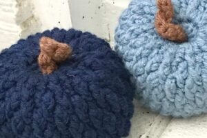 Knitted pumpkin ornaments in navy and light blue with brown stems, perfect for fall decorations.