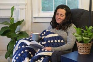 Woman relaxing with blanket and coffee in a cozy indoor setting.