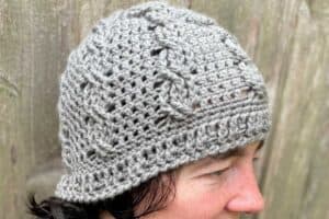 Knit gray beanie with cable pattern on a woman outdoors.