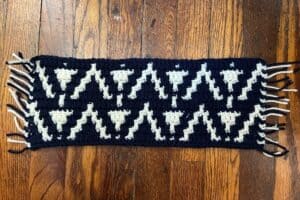 Handwoven black and white geometric patterned scarf on wooden floor.