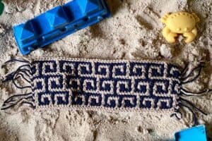Beach toy and towel on sandy surface with seashells and toys.