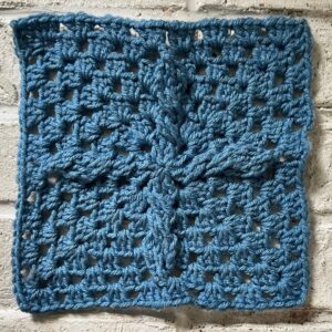 Crochet butterfly motif square in blue yarn, showcasing intricate stitch work.
