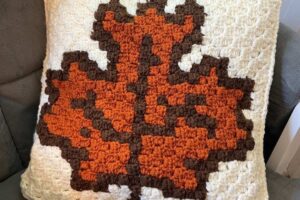 Handcrafted pillow featuring a pixelated autumn maple leaf design in orange, brown, and white.