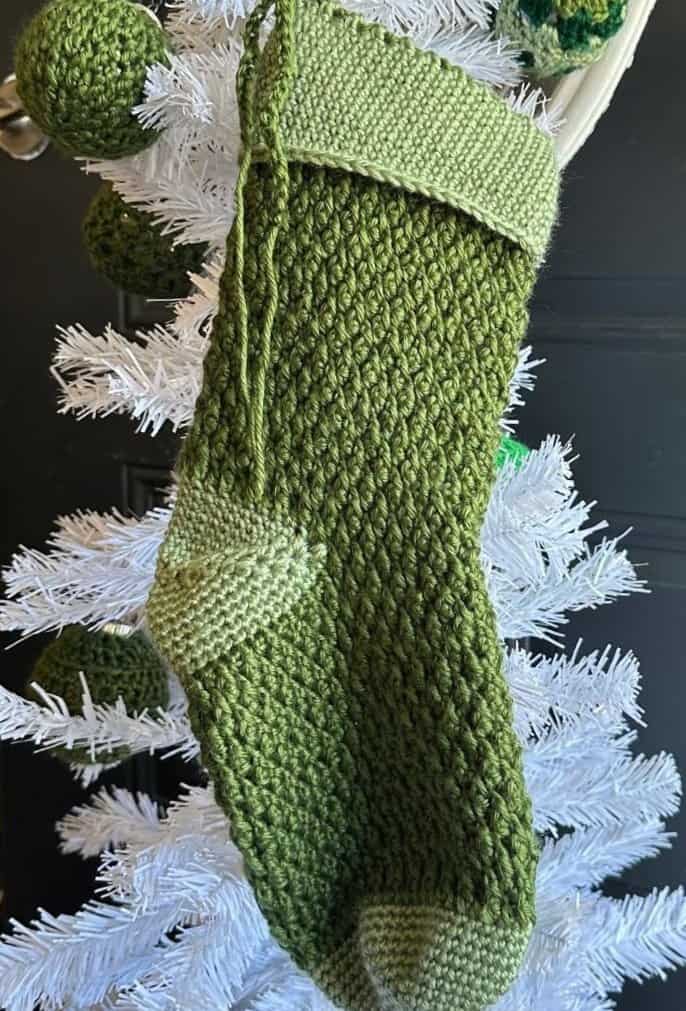 Handmade green alpine crochet stocking with textured pattern for Christmas decor.