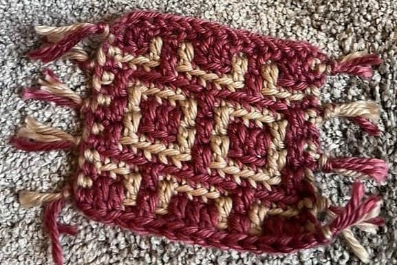 Mosaic crochet coaster with geometric square pattern in red and beige yarn.