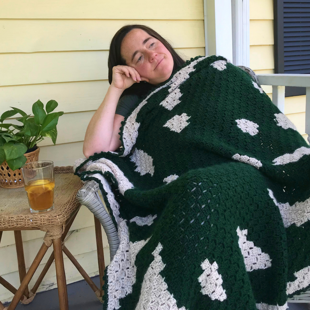 Woman on a porch covered by a monstera leaf plant C2C blanket.