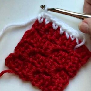 Red knitted fabric with white edging and crochet hook for crafting or knitting projects.