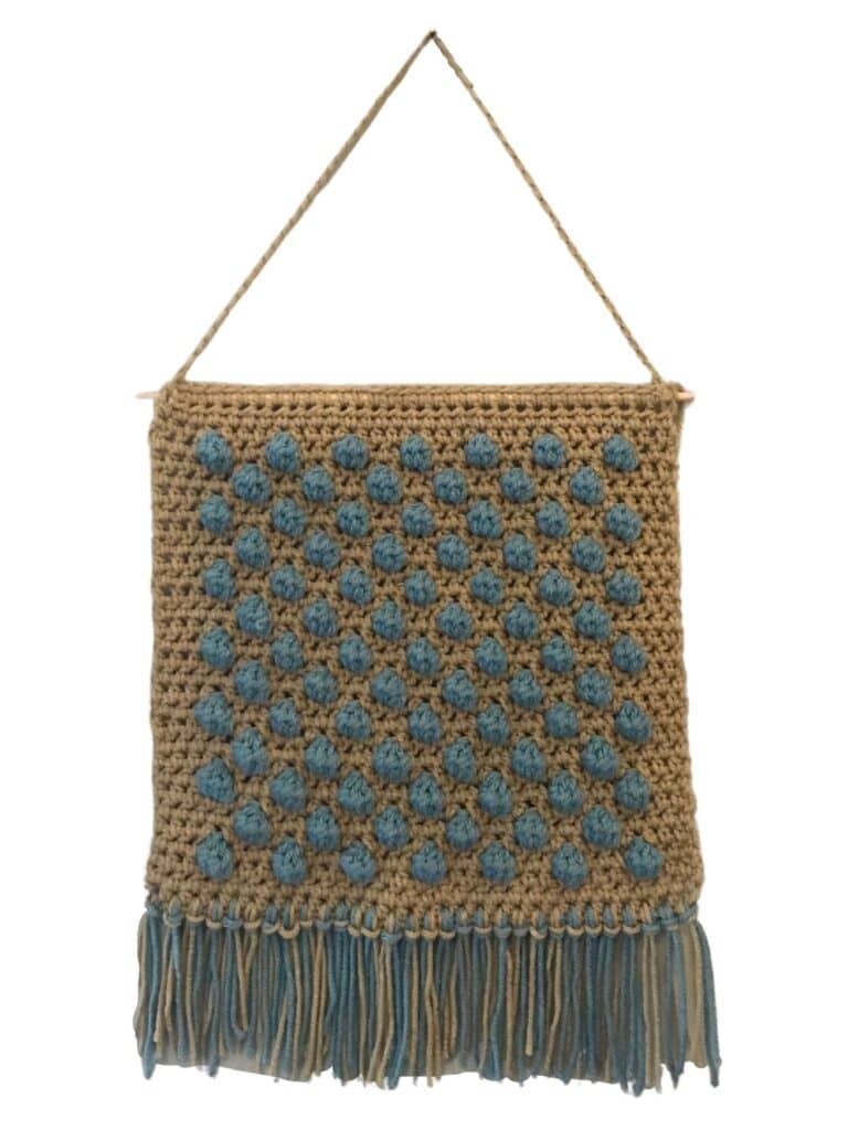 Crochet wall hanging featuring blue textured dots and fringe detail, perfect for home decor.