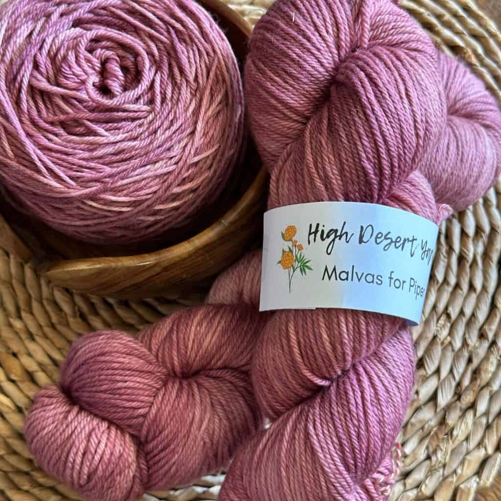 Pink yarn skeins and a ball of yarn in a woven basket.