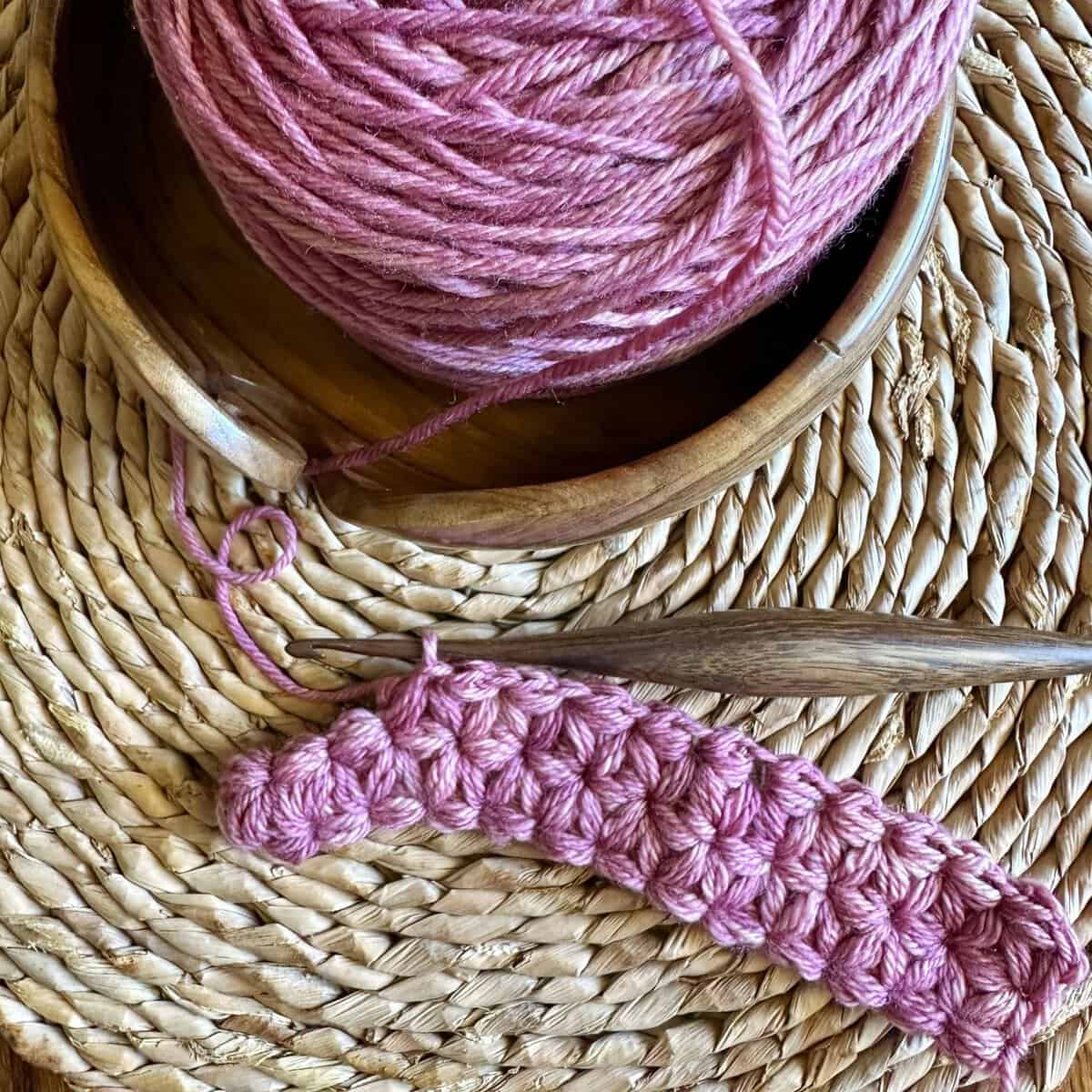 Yarn and crochet hook for knitting or crochet projects on a textured woven background.