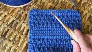 Hand knitting with blue yarn on a textured woven surface.