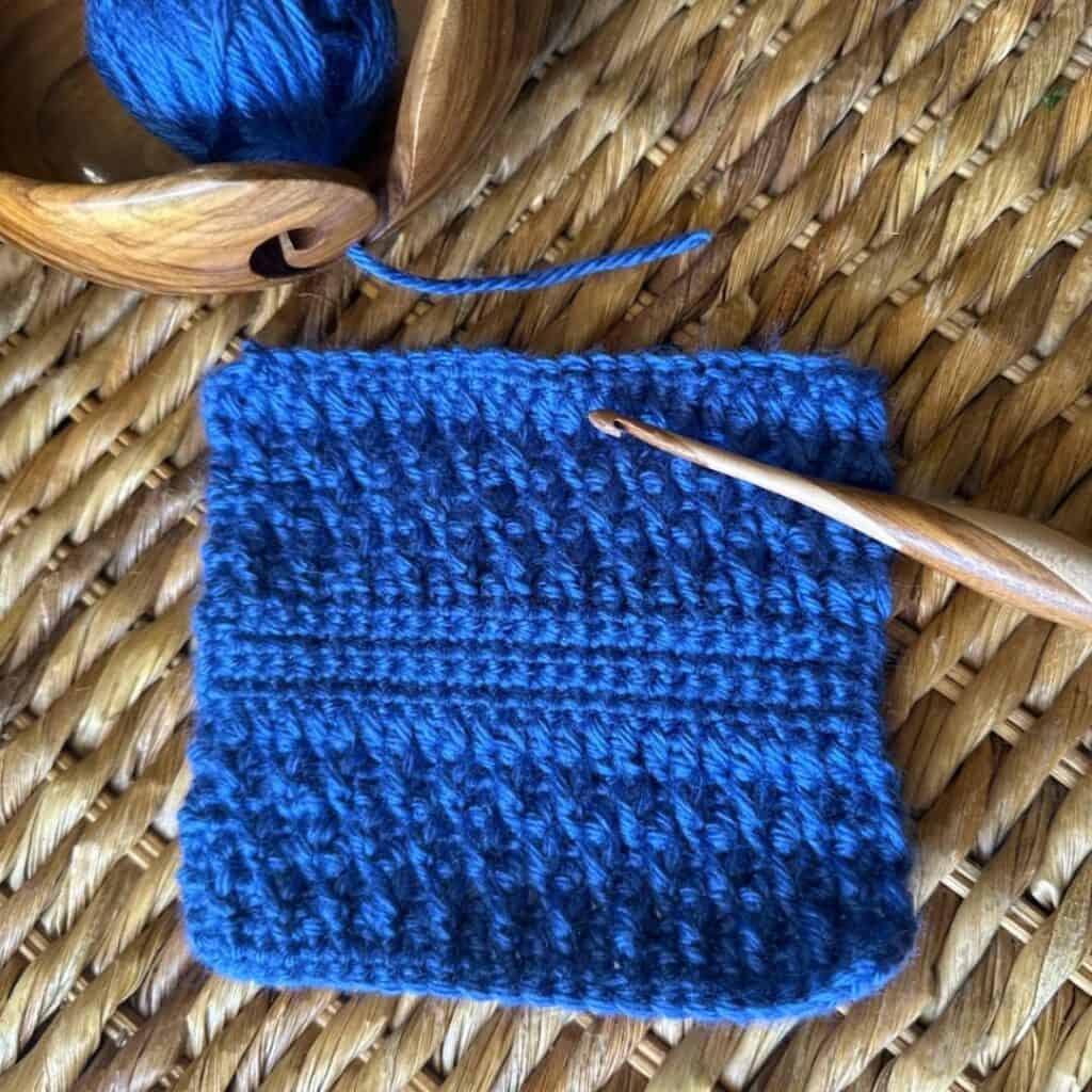Knitting project featuring vibrant blue yarn and a wooden knitting needle on a woven surface.