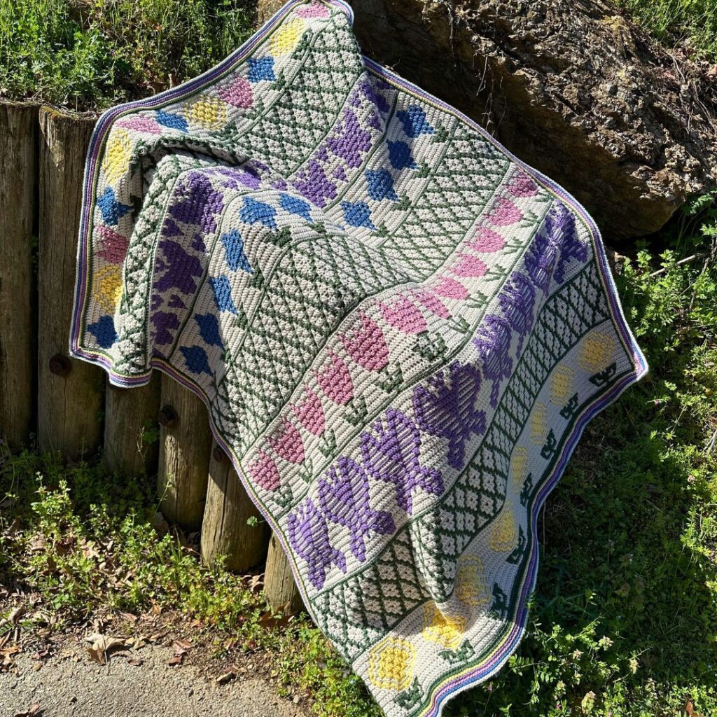A springtime mosaic crochet blanket featuring pastel colors with images of flowers and butterflies.
