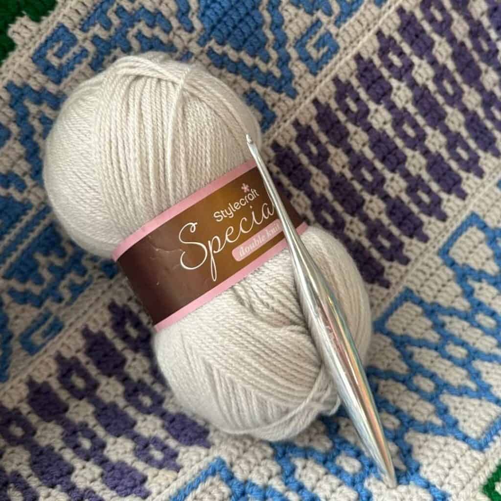 A skein of StyleCraft Special DK, the suggested yarn for the geometric mosaic crochet blanket, shown on a section of the blanket