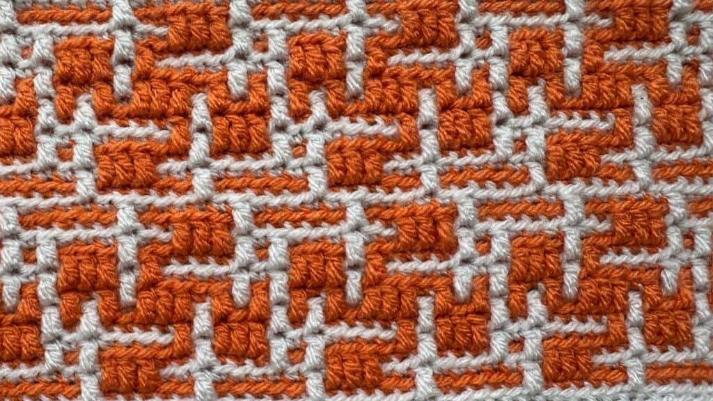 Close-up of a geometric mosaic crochet blanket with orange and white patterns.