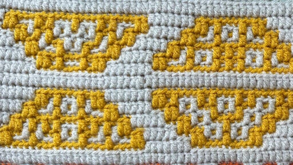 Close-up of a geometric mosaic crochet blanket with yellow and gray patterns.
