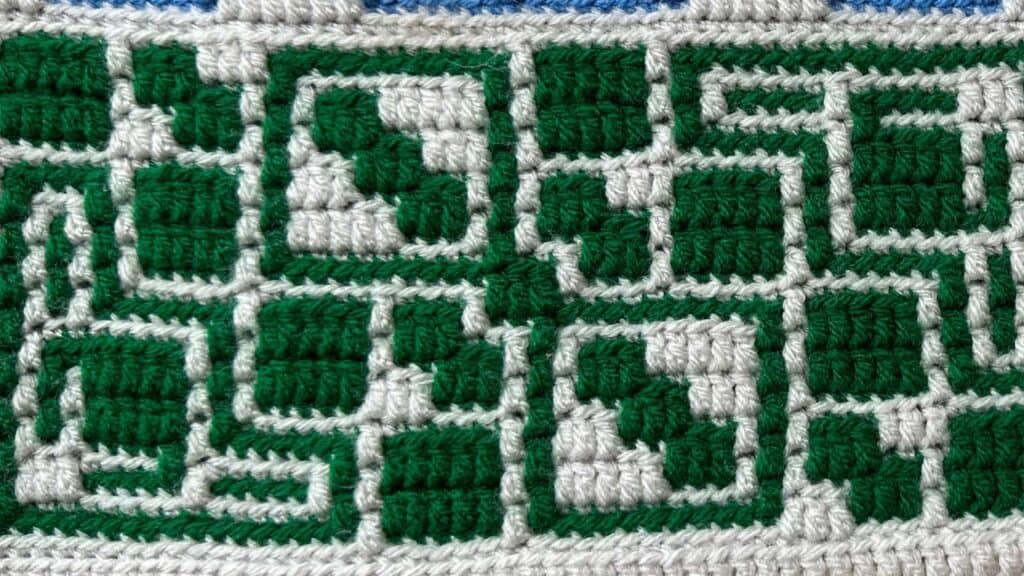 Close-up of a geometric mosaic crochet blanket with green and white patterns.