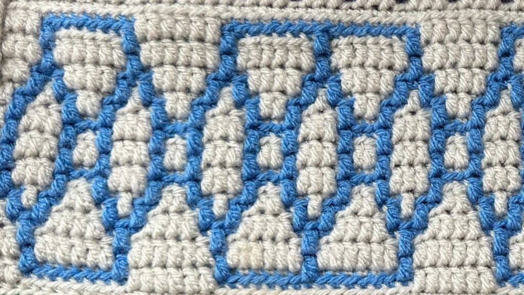Close-up of a geometric mosaic crochet blanket with blue and beige yarns.