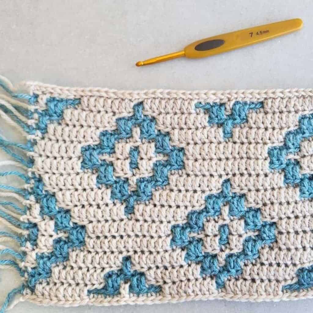 Close-up of a geometric mosaic crochet blanket with blue and white yarns.