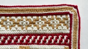 Close-up of a mosaic crochet gingerbread blanket with red, white, and gold yarns.