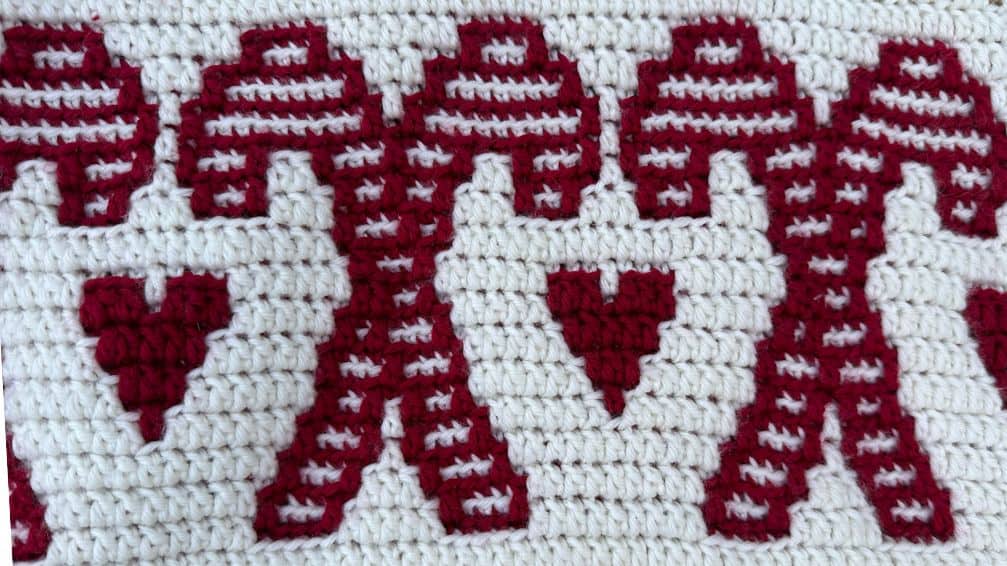 Close-up of a festive gingerbread-themed crochet blanket with red and white yarn.