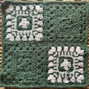 Handmade crochet granny square blanket with white and green yarns.