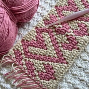 Crocheted mosaic heart blanket strip with pink and cream yarns.