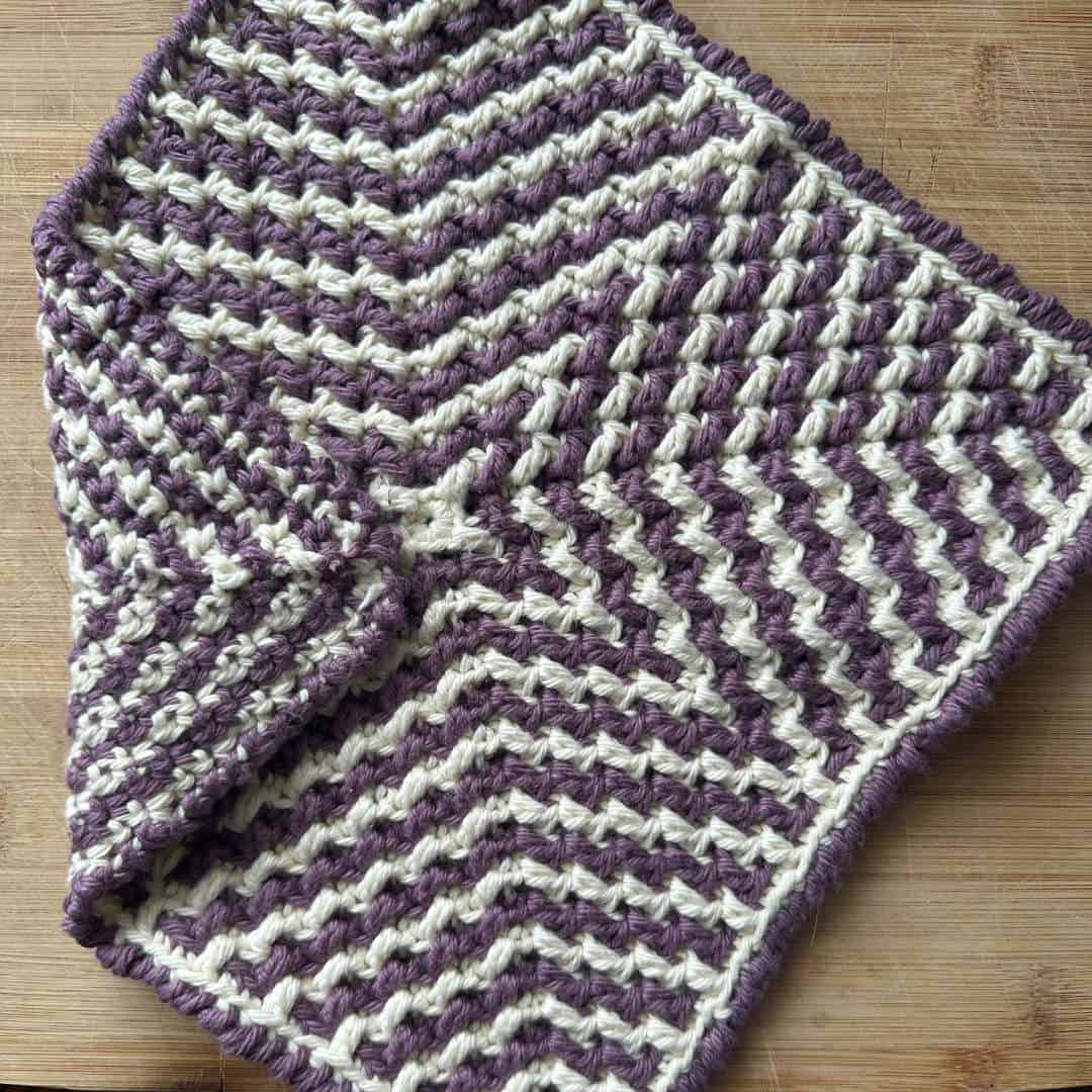 Close-up of a purple and white mosaic crochet starburst washcloth on wood surface.