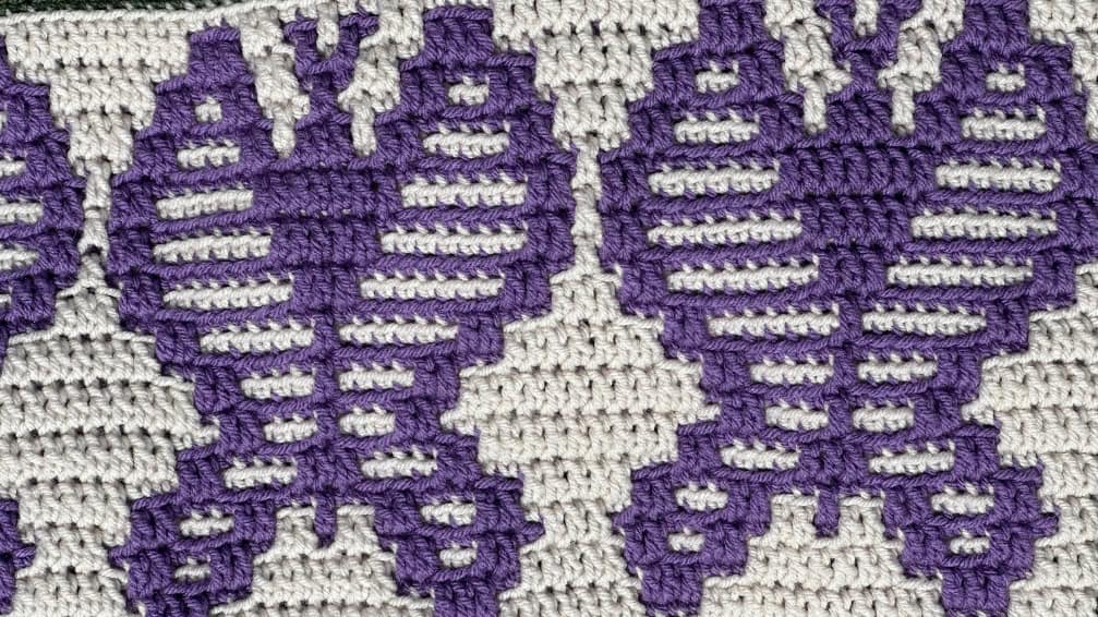 Detailed mosaic crochet sunflower pattern in purple and beige yarns.